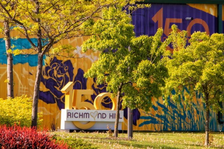 Colorful outdoor mural and signage celebrating Richmond Hill’s 150th anniversary, surrounded by trees and landscaped greenery.