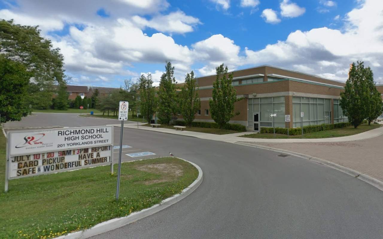 Richmond Hill High School entrance with smooth asphalt roadway, sidewalks, and school buildings under a bright summer sky in Richmond Hill, Ontario.
