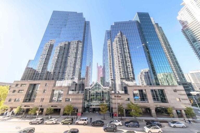Modern high-rise office and condominium towers in North York Centre, Toronto, featuring reflective glass facades, street-level retail spaces, and busy urban traffic in a prominent commercial and residential district.