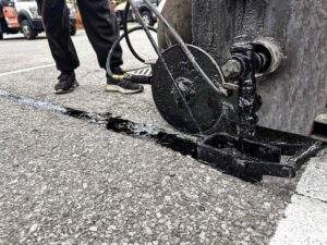 Close-up of a crack filling machine applying hot rubberized sealant to an asphalt pavement crack, helping prevent water infiltration and extending the lifespan of a commercial parking lot surface.