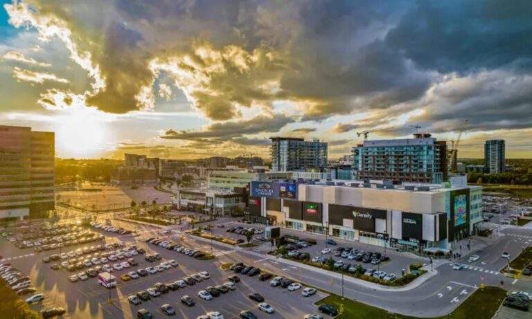 Aerial view of downtown Markham featuring a busy commercial district, large parking lots, modern retail buildings, and surrounding residential and office developments at sunset.