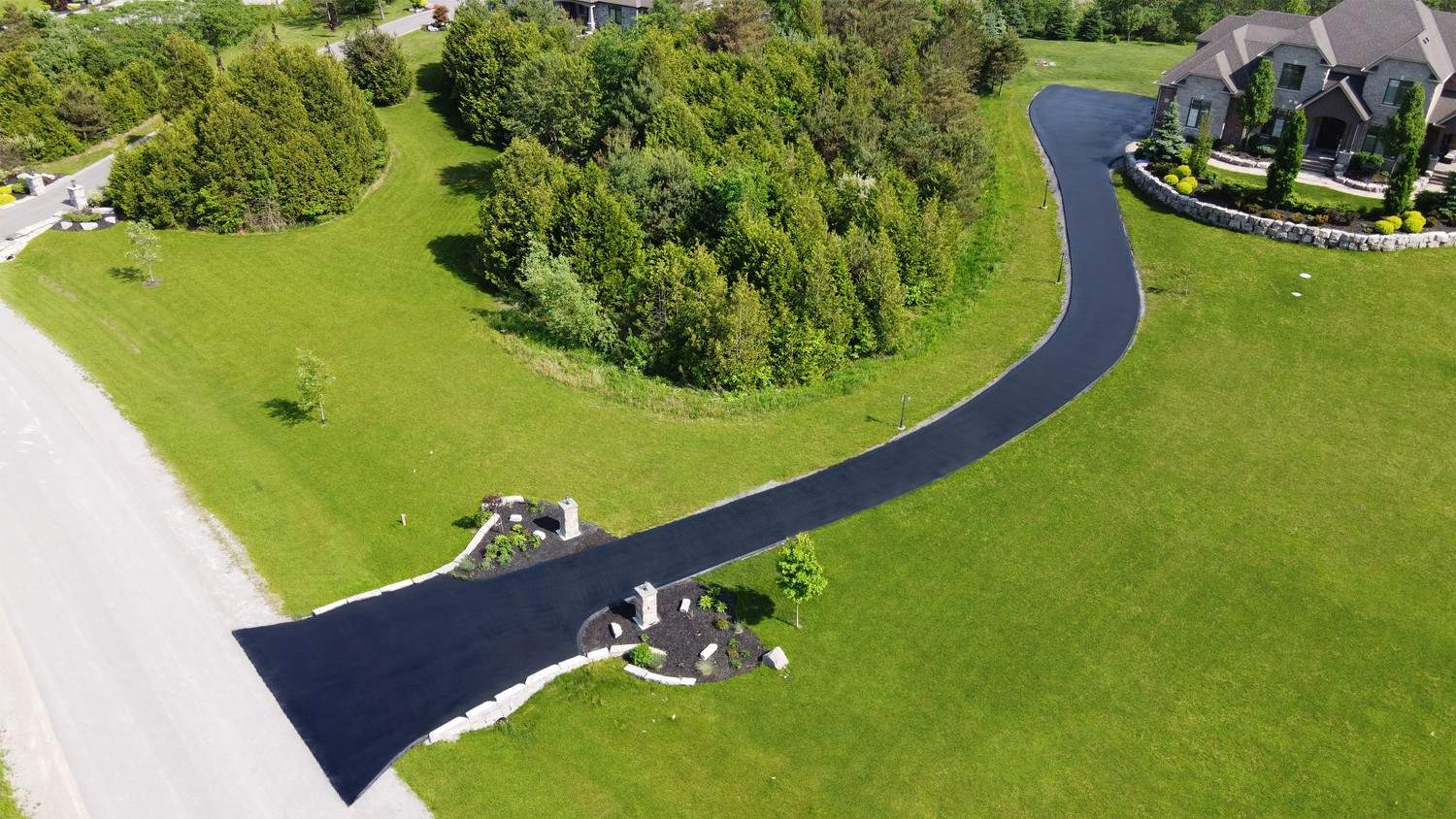 Aerial view of a long, freshly paved blacktop driveway leading to a luxury home