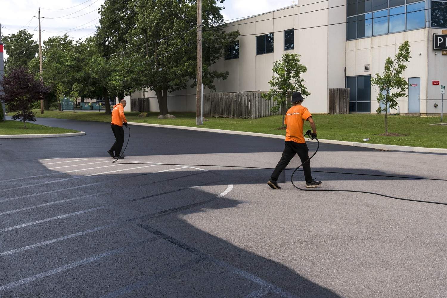 Action Paving technicians spraying protective blacktop sealcoating onto a commercial parking lot in Ajax ON.
