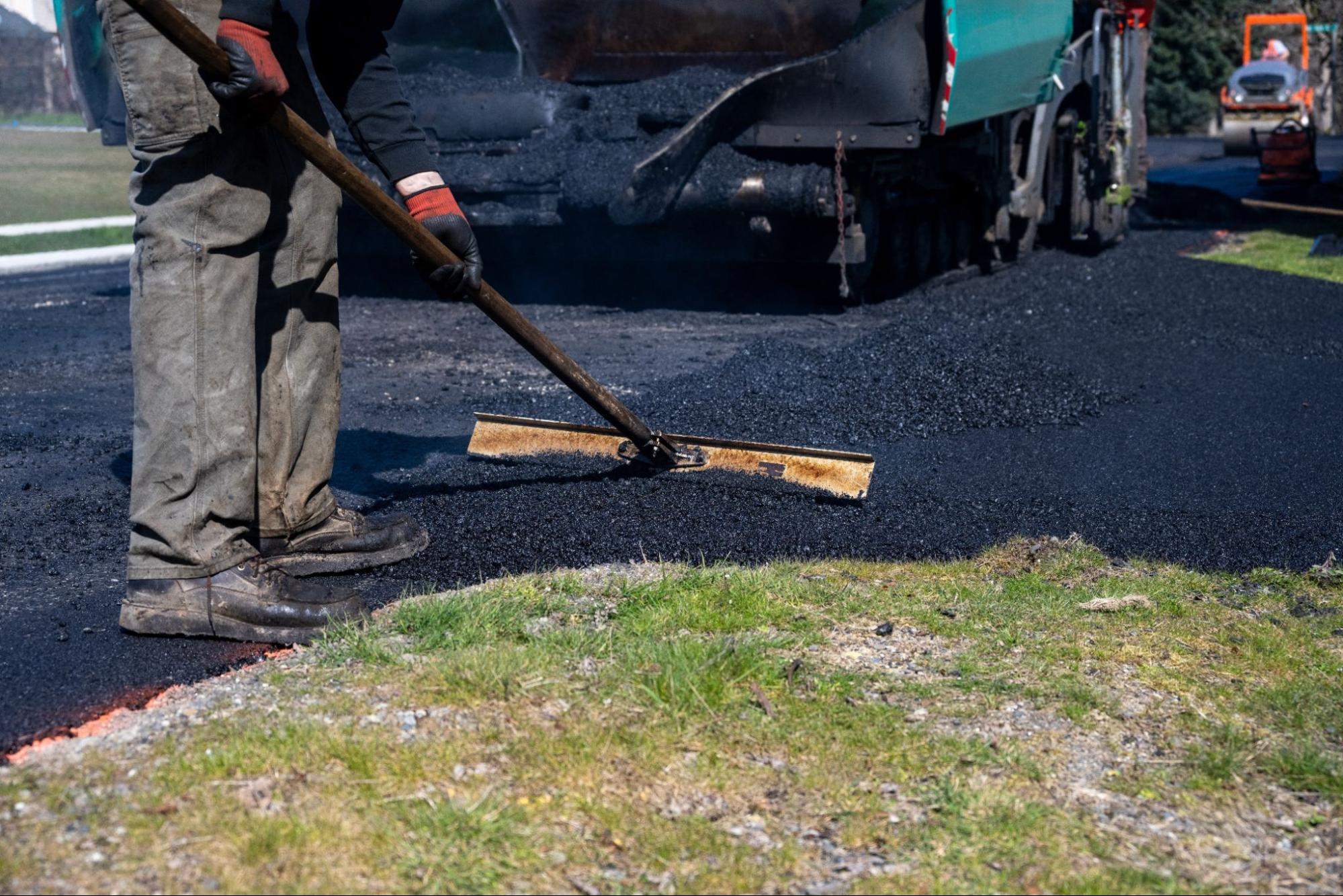 Paving worker using a lute rake to level fresh asphalt during fall driveway and parking lot repairs 